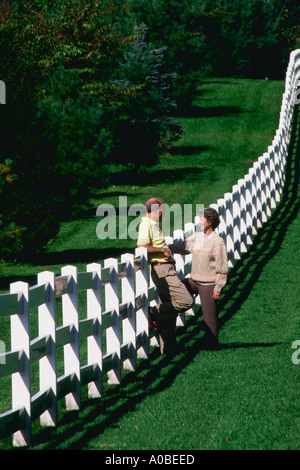 Mittleren gealterten paar machen Sie eine Pause von einem entspannenden Spaziergang, lehnen Sie sich gegen eine weiße Holzzaun und chatten in Maryland Stockfoto
