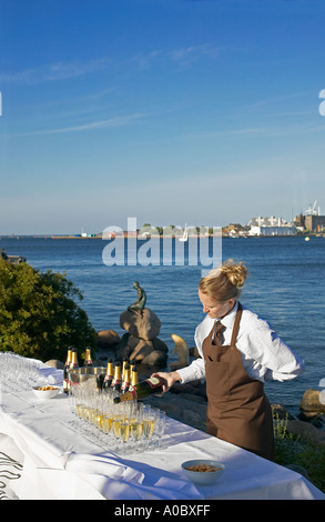 Junge Frau, die neben der Statue der Kleinen Meerjungfrau Gläser mit Champagner füllt, Kopenhagen, Dänemark, Europa Stockfoto