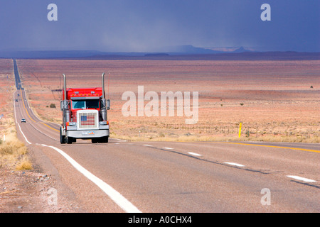 Rote LKW mit einer amerikanischen Flagge auf den kühleren Laufwerken auf einer langen geraden Autobahn durch die Painted Desert im nördlichen Arizona Stockfoto