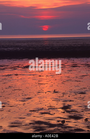 untergehende Sonne und ihre Reflexion mit Wolken auf nassen sandigen Strand West Norfolk NORFOLK EAST ANGLIA ENGLAND UK Stockfoto