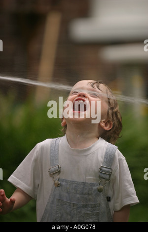 Lewis im Alter von zwei spielen mit dem Gartenschlauch im Garten Stockfoto