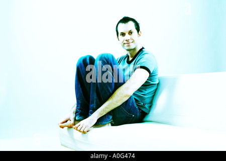 Junger Mann auf einem Sofa sitzt und schaut in die Kamera Stockfoto