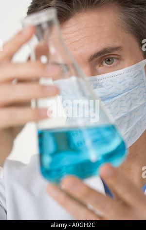 Maskierte Wissenschaftler untersuchen blaue Flüssigkeit Stockfoto