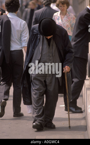 Senior man 1980s London, Großbritannien. Er trägt einen Melonenhut und verwendet einen Spazierstock, der auf einer überfüllten Straße läuft, und hat einen Höcker von Auswanderern. HOMER SYKES Stockfoto