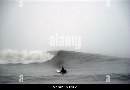 Einsamer Surfer an einem nebeligen Tag in Rest Bay Porthcawl, South Wales Stockfoto