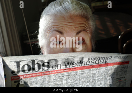 Überrascht aussehende Frau Rentner einen Überblick über die angebotenen Arbeitsplätze in ihrer Lokalzeitung. Stockfoto