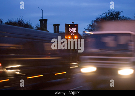 eine blinkende Geschwindigkeit Warnzeichen und schnell bewegenden Feierabendverkehr durch das Dorf große Barton in Suffolk, UK Stockfoto