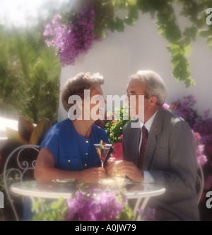 im Ruhestand Alter paar, trinken einen Cocktail und Wein auf Reben bedeckt Terrasse im Sonnenschein Stockfoto