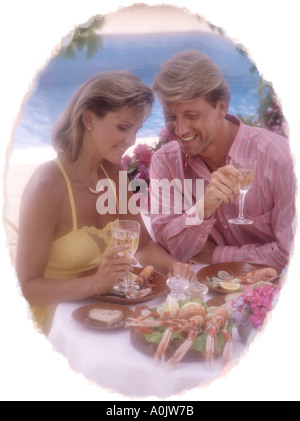 jung, Ehepaar mittleren Alters essen Meeresfrüchte im Abendlicht auf Terrasse mit Pool Oval vignette Stockfoto