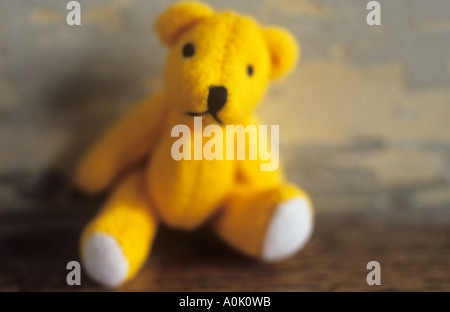 Nahaufnahme eines gelben Teddybär sitzend auf einem Holztisch oder Felsvorsprung mit einem Peeling Blau-Creme-Wand hinter Stockfoto