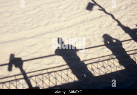 Schatten werfen auf weichen, weißen Sand des Mannes stützte sich auf Geländer und Frau Foto und Meer Teleskop und Lichtmast Stockfoto