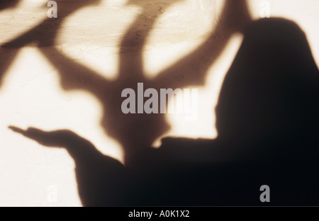 Schatten des monklike Kapuzengestalt streckte seine Hand mit der Handfläche nach oben vor den Schatten des reich verzierten klaren Kirchenfenster Stockfoto