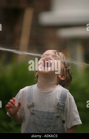 Lewis im Alter von zwei spielen mit dem Gartenschlauch im Garten Stockfoto