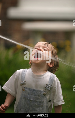 Lewis im Alter von zwei spielen mit dem Gartenschlauch im Garten Stockfoto