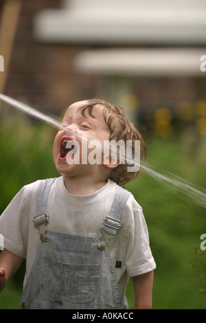 Lewis im Alter von zwei spielen mit dem Gartenschlauch im Garten Stockfoto