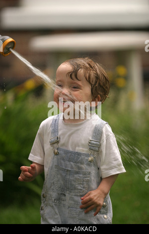 Lewis im Alter von zwei spielen mit dem Gartenschlauch im Garten Stockfoto