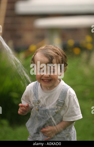 Lewis im Alter von zwei spielen mit dem Gartenschlauch im Garten Stockfoto