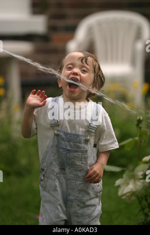 Lewis im Alter von zwei spielen mit dem Gartenschlauch im Garten Stockfoto