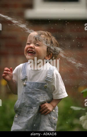 Lewis im Alter von zwei spielen mit dem Gartenschlauch im Garten Stockfoto
