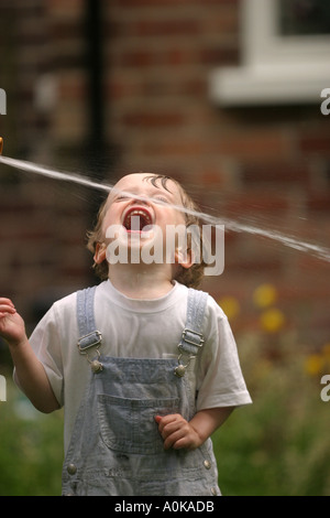 Lewis im Alter von zwei spielen mit dem Gartenschlauch im Garten Stockfoto
