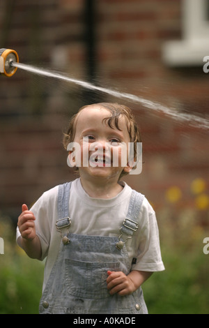 Lewis im Alter von zwei spielen mit dem Gartenschlauch im Garten Stockfoto