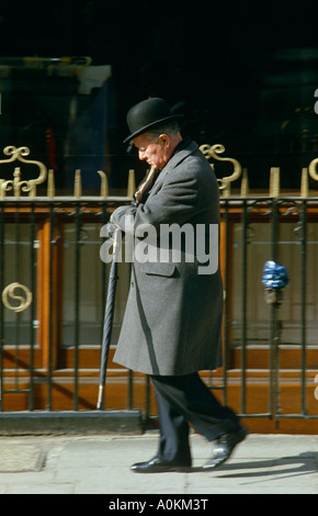 Ein alten englischer Gentleman mit Melone und Brolly Spaziergänge in der Wintersonne in Mayfair, London UK Stockfoto