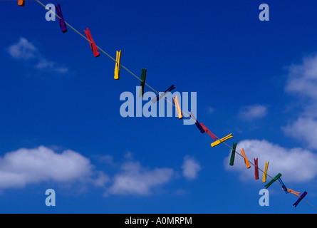 Mehrfarbige Wäscheklammern, die an einer Wäscheleine mit weißen Wolken hängen Und blauer Himmel Stockfoto