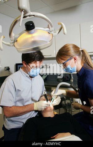 Zähne und Zahnfleisch Behandlung durch einen Zahnarzt und seine Assistentin an einem Patienten in einem Zahnarzt-Stuhl in einer Zahnarztpraxis Stockfoto