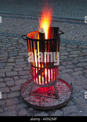 Protokolle in einem schmalen Metall Kohlenbecken auf einer gepflasterten Straße heftig brennen. Stockfoto