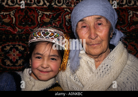 Usbekistan. Alte Frau und kleine Mädchen mit Teppich Wandbehang hinter. Stockfoto