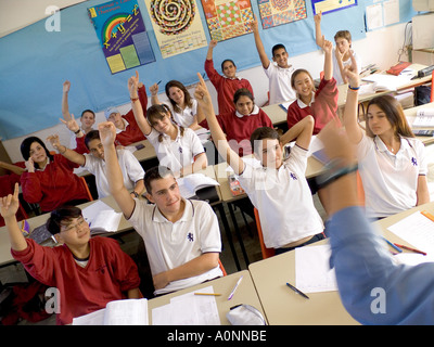 Blick über Lehrer Schulter zu enthusiastischen älteren multikulturellen Jugendlichen Studenten mit Händen oben in der Schule Klassenzimmer Stockfoto