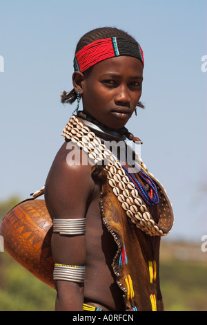 Hamer Dame tragen traditionelle Ziegenfell Kleid verziert mit Cowie Schalen tragen Kalash auf ihrem Weg zum Djombo Dorf Markt Stockfoto