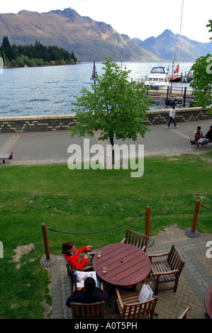 Touristen mit einem Bier am Ufer des Lake Wakatipu Queenstown Neuseeland Nein Herr entspannend Stockfoto