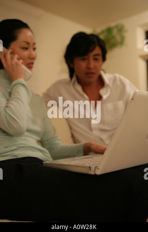 Junge Frau telefonieren mit einem Handy und benutze ein Laptop mit einem jungen Mann neben ihr sitzen Stockfoto