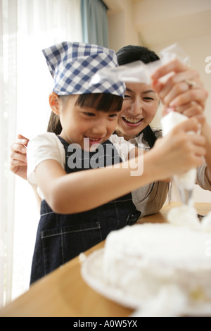 Mitte Erwachsene Frau und ihrer Tochter einen Kuchen dekorieren Stockfoto