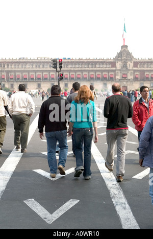 Menschen überqueren Sie die Straße an einem Fußgängerüberweg in Plaza De La Constitución-Mexiko-Stadt mit Nationalpalast hinter Stockfoto