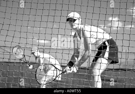 Zwei Mädchen spielen Doppel im Tennis an einem heißen sonnigen Tag, gesehen durch das Netz in schwarz und weiß Stockfoto