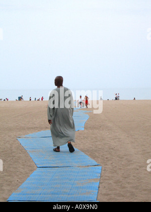 Afrikanische amerikanische Mann trägt ein Gewand zu Fuß auf einem Pfad am Strand Stockfoto