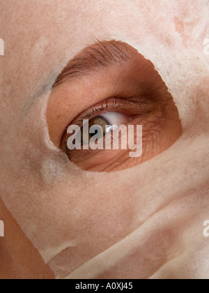 Auge von einer Frau mittleren Alters, Blick durch ein Loch in ein Blatt Schönheitsmaske während der Behandlung Stockfoto