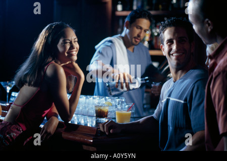 Zwei junge Männer und eine junge Frau in einer Bar mit Barkeeper Gießen Wein hinter ihnen zu begegnen Stockfoto