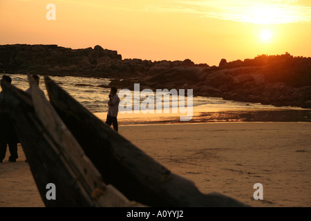 Männer am Kovalam Beach bei Sonnenuntergang mit traditionellen Fischerboot im Vordergrund Stockfoto