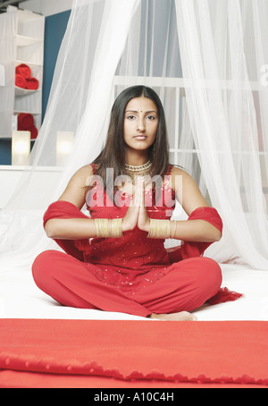 Porträt einer jungen Frau in einem Gebet Position auf dem Bett sitzend Stockfoto