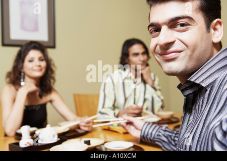 Porträt eines jungen Mannes, der mit seinen Freunden am Esstisch sitzen Stockfoto
