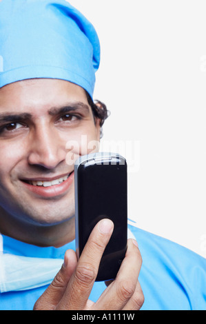 Porträt eines männlichen Arztes trägt chirurgische Peelings und hält ein Mobiltelefon Stockfoto