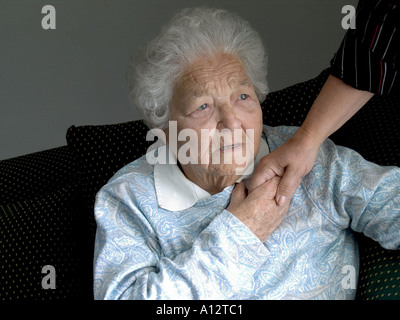 Ängstliche ältere Dame, die zu Hause sitzt, hält die beruhigende Hand der fürsorglichen taktilen Betreuerin in natürlichem Licht Innenraum] Landschaft Stockfoto