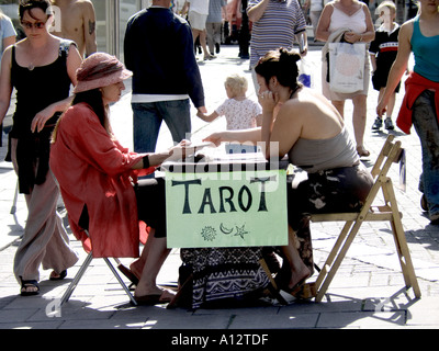 Tarot Kartenleser im Freien in der High Street verlost ihren einzigartigen Handel mit einem Kunden, der eine Karte im Zentrum einer belebten sonnigen High Street in Großbritannien auswählt Stockfoto