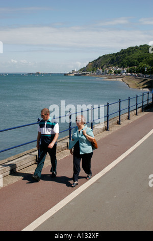 TOURISTEN FLANIEREN ENTLANG DER PROMENADE MIT MUMBLES PIER IM HINTERGRUND, SWANSEA, WEST GLAMORGAN, SOUTH WALES, GROßBRITANNIEN Stockfoto