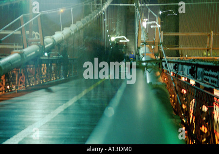 Walker gefangen in Bewegung auf eine lange Exposition der Brooklyn Bridge walkway, New York, USA Stockfoto