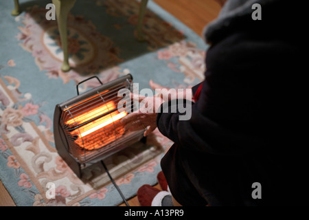 Ältere Frau hält warm durch das sitzen in der Nähe von traditionellen elektrischen Feuer in häuslicher Umgebung Stockfoto