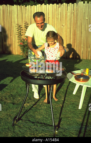 Ein Mann hilft ein kleines Mädchen Hamburger außerhalb auf einem Holzkohlegrill im Garten kochen Stockfoto